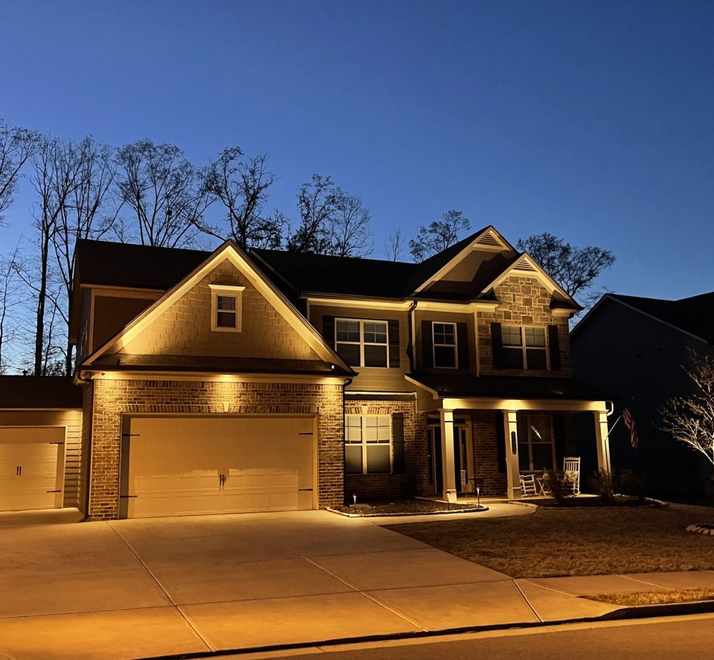 Exterior view of a home with landscape lighting highlighting architectural features. Buford, GA